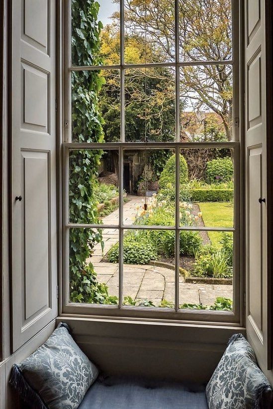Timber sash window with panelled shutters and window seat overlooking a walled London garden